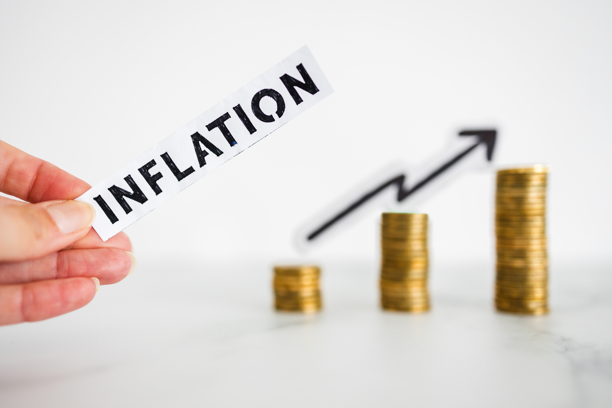 A hand holding a sign with the word inflation on top of a stack of coins.