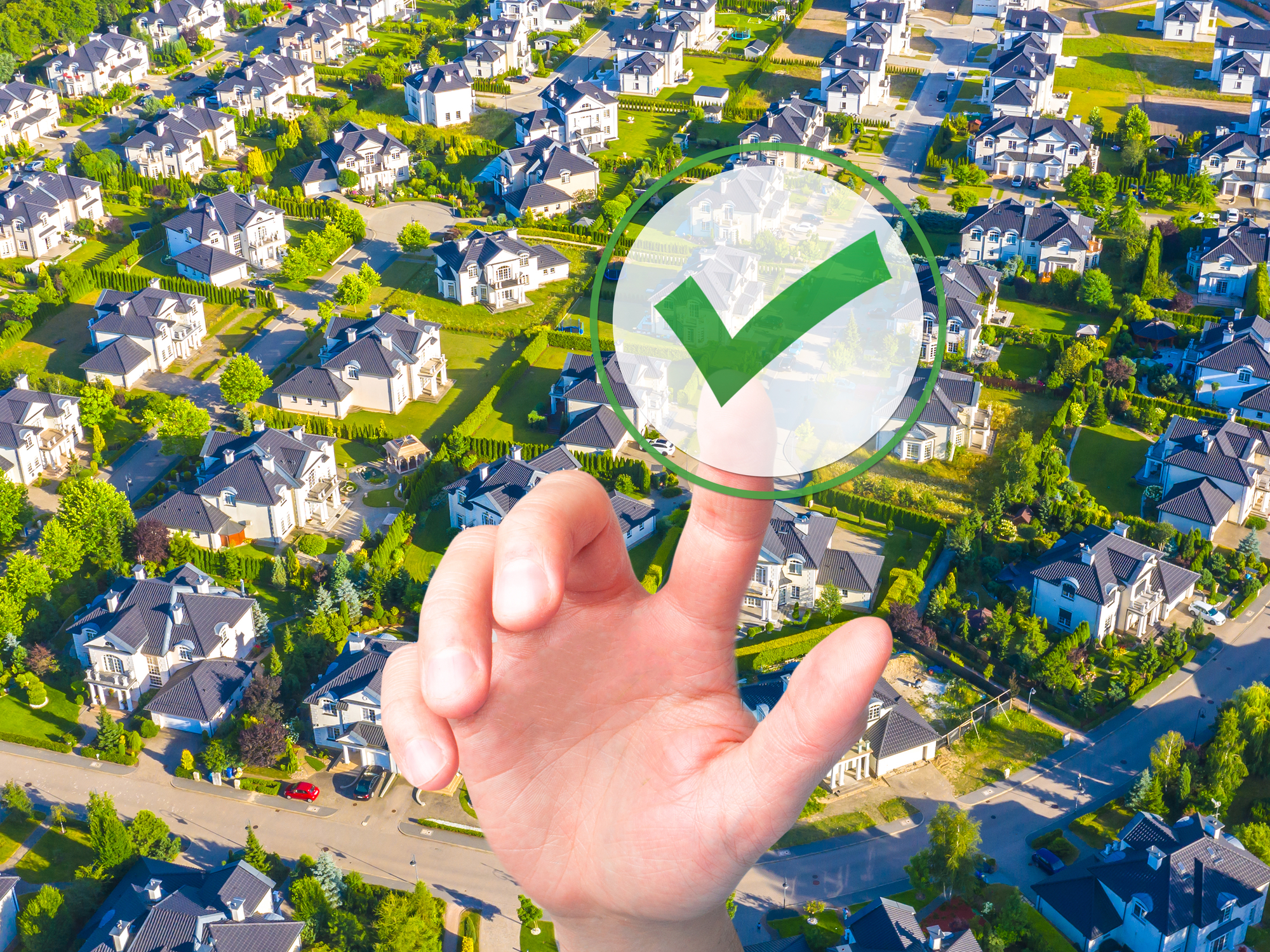 A hand is pointing at a green check mark in front of a residential neighborhood.