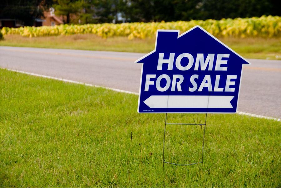 A home for sale sign in front of a field.