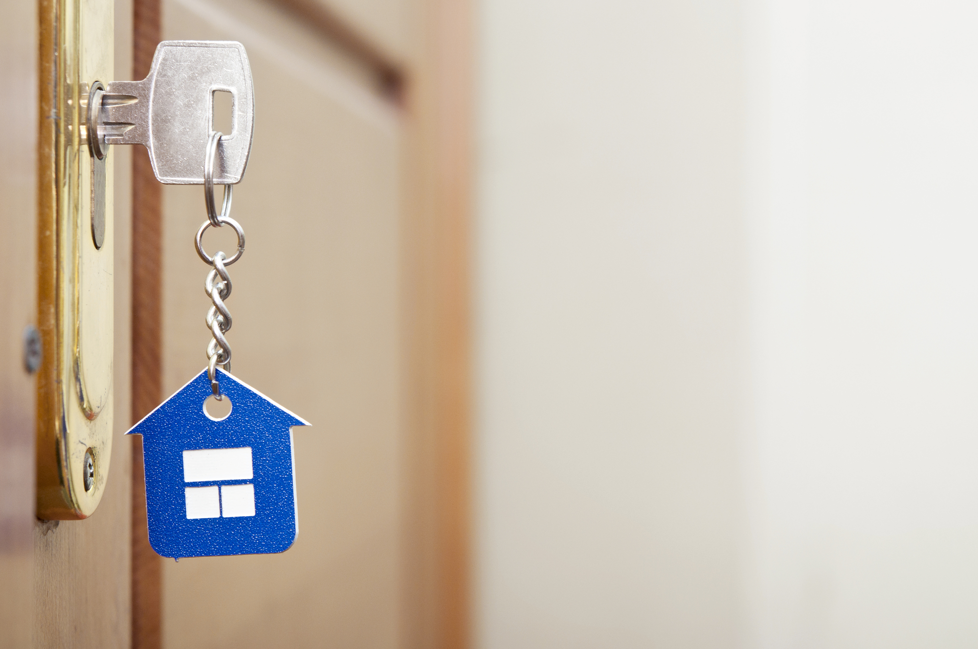 A blue house key hangs on a wooden door.