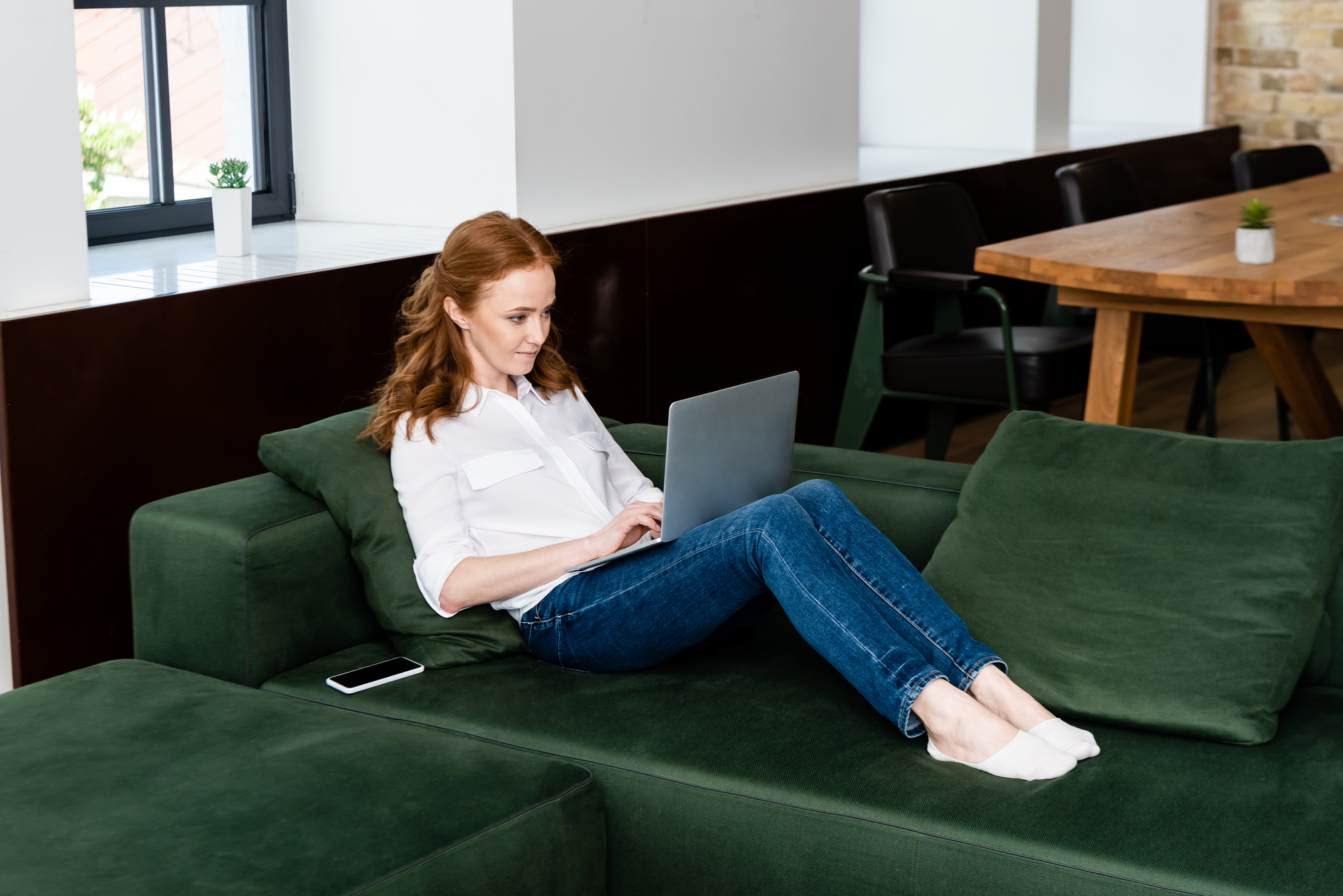 A woman sitting on a green couch with a laptop.