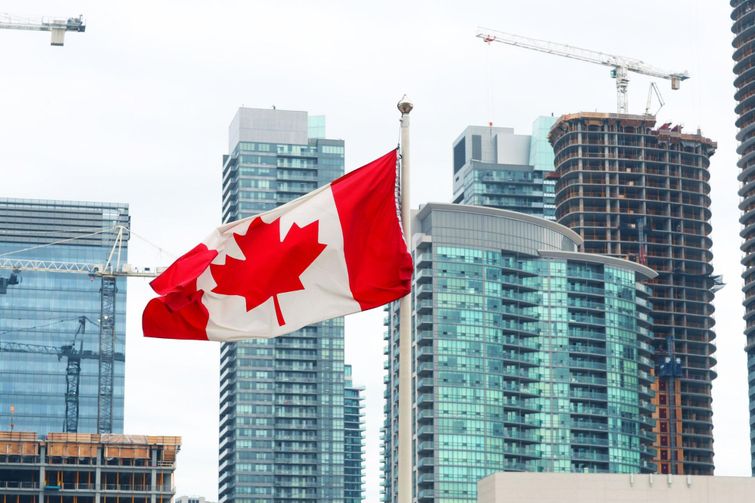 A canadian flag flies in front of tall buildings.
