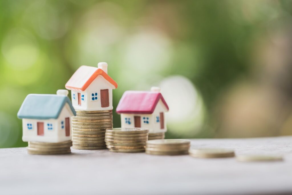 Miniature house on a stack of coins with blurred background.