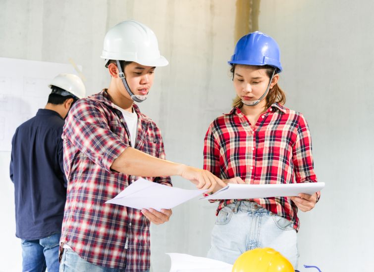 Two people in hard hats are investly examining blueprints.