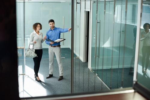 Two people standing in an office with glass walls.
