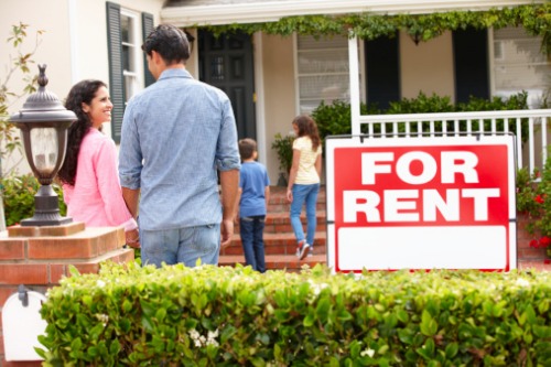 A family standing in front of a house with a for rent sign.