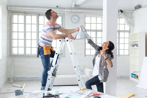 A man and woman standing on a ladder in a white room.