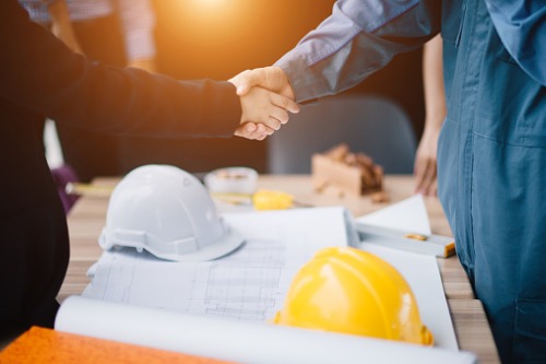 Two construction workers shaking hands in front of blueprints.