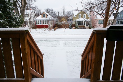A view of a snow covered backyard from a wooden deck.