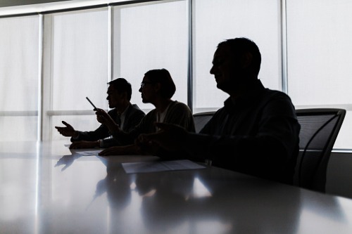 Silhouettes of business people sitting at a conference table.