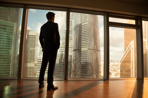 A businessman looking out of a window at a cityscape.