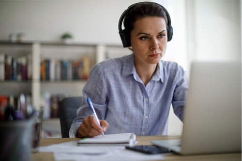 A woman wearing headphones is sitting at a desk with a laptop.
