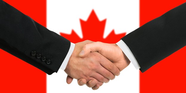 Two businessmen shaking hands in front of a canadian flag.