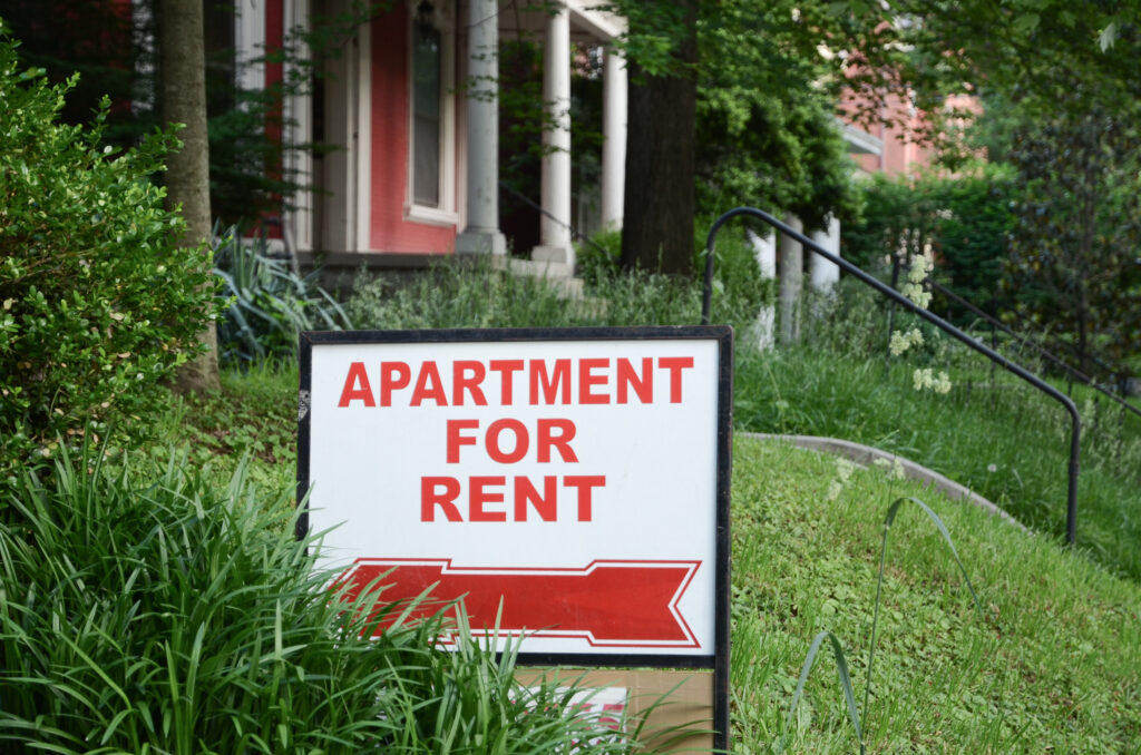 An apartment for rent sign in front of a house.