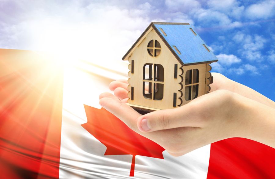 A hand holding a house model in front of a canadian flag.