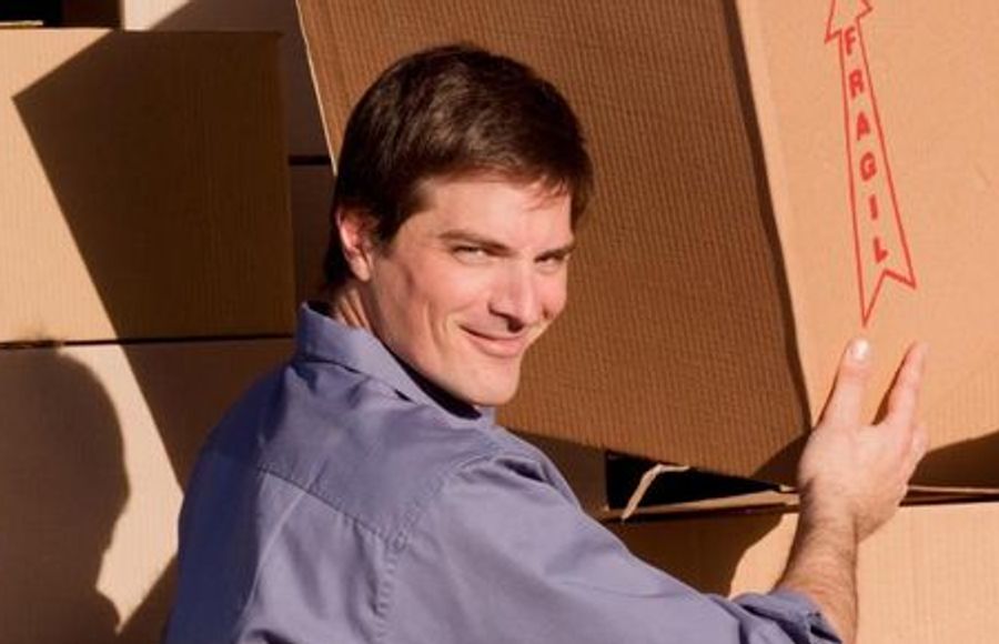 A man holding a moving box in front of a moving truck.