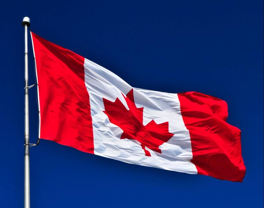 A canadian flag flying in the wind against a blue sky.
