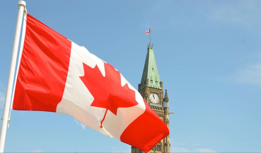 A canadian flag flies in front of a clock tower.