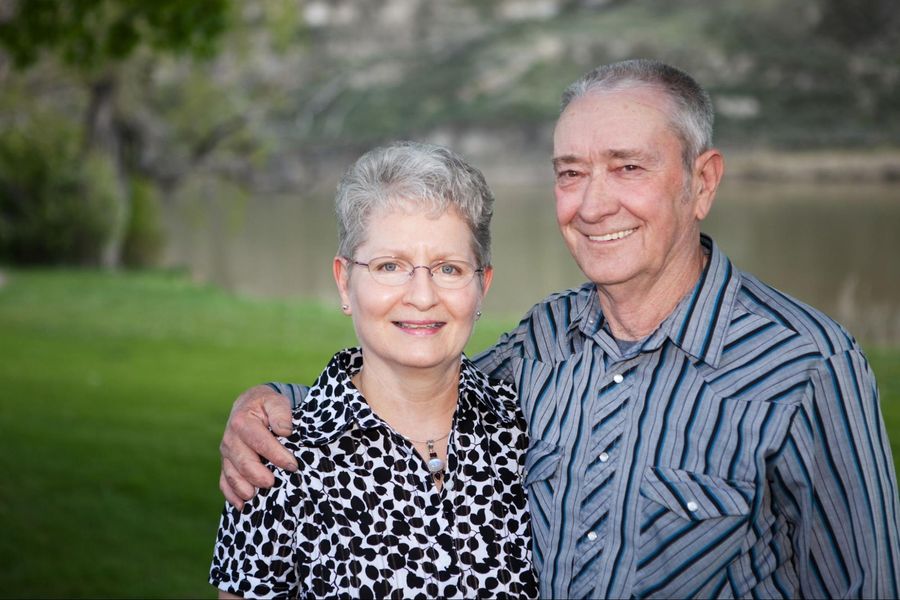 An older couple posing for a photo in front of a lake.