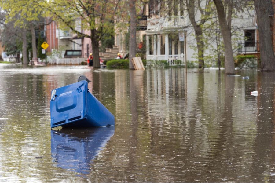 A blue trash can sits in a flooded street.