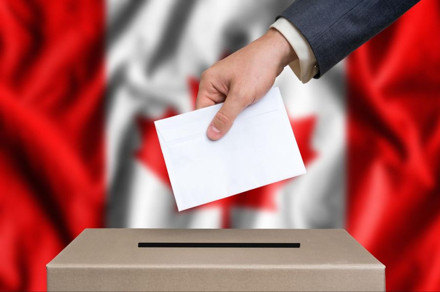 A man is putting a paper into a voting box in front of a canadian flag.