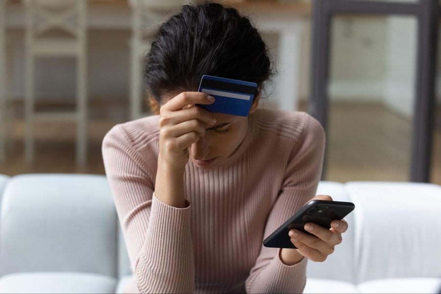 A woman holding a credit card while looking at her phone.