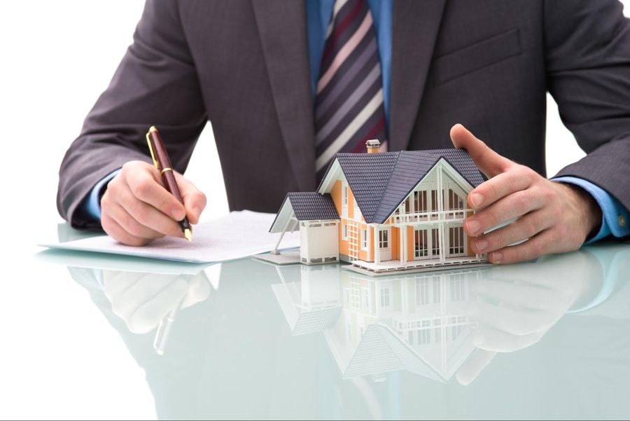 A man in a suit is holding a model of a house and writing on a piece of paper.