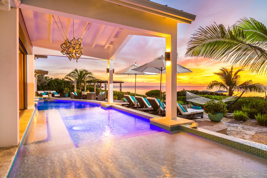 A pool with lounge chairs and a sunset view.