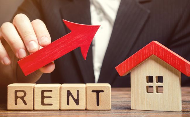 A businessman holding a wooden block with the word rent and a red arrow.