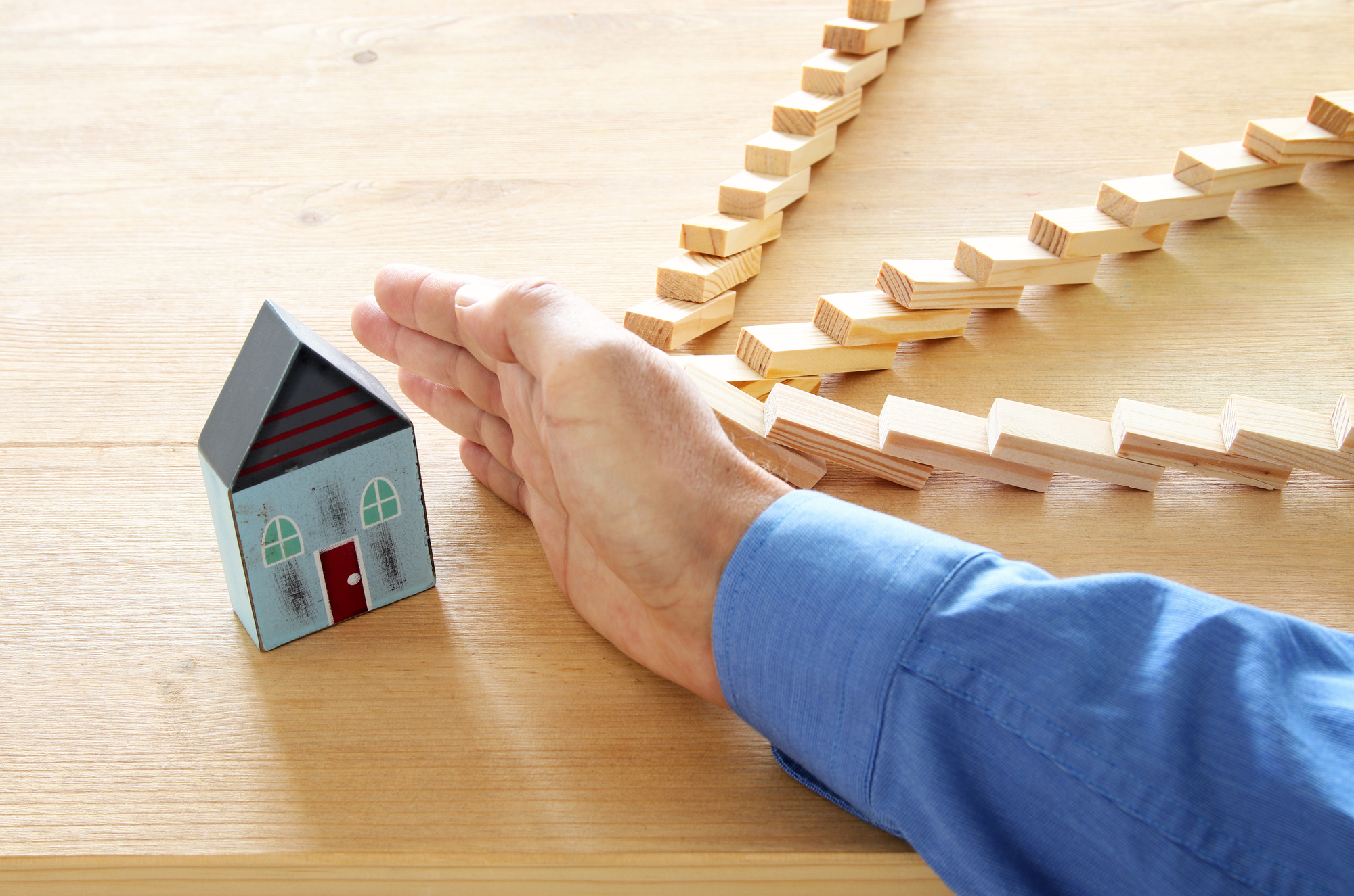 concept image of real estate insurance and protection. man hands blocking the domino effect, saving a small house.