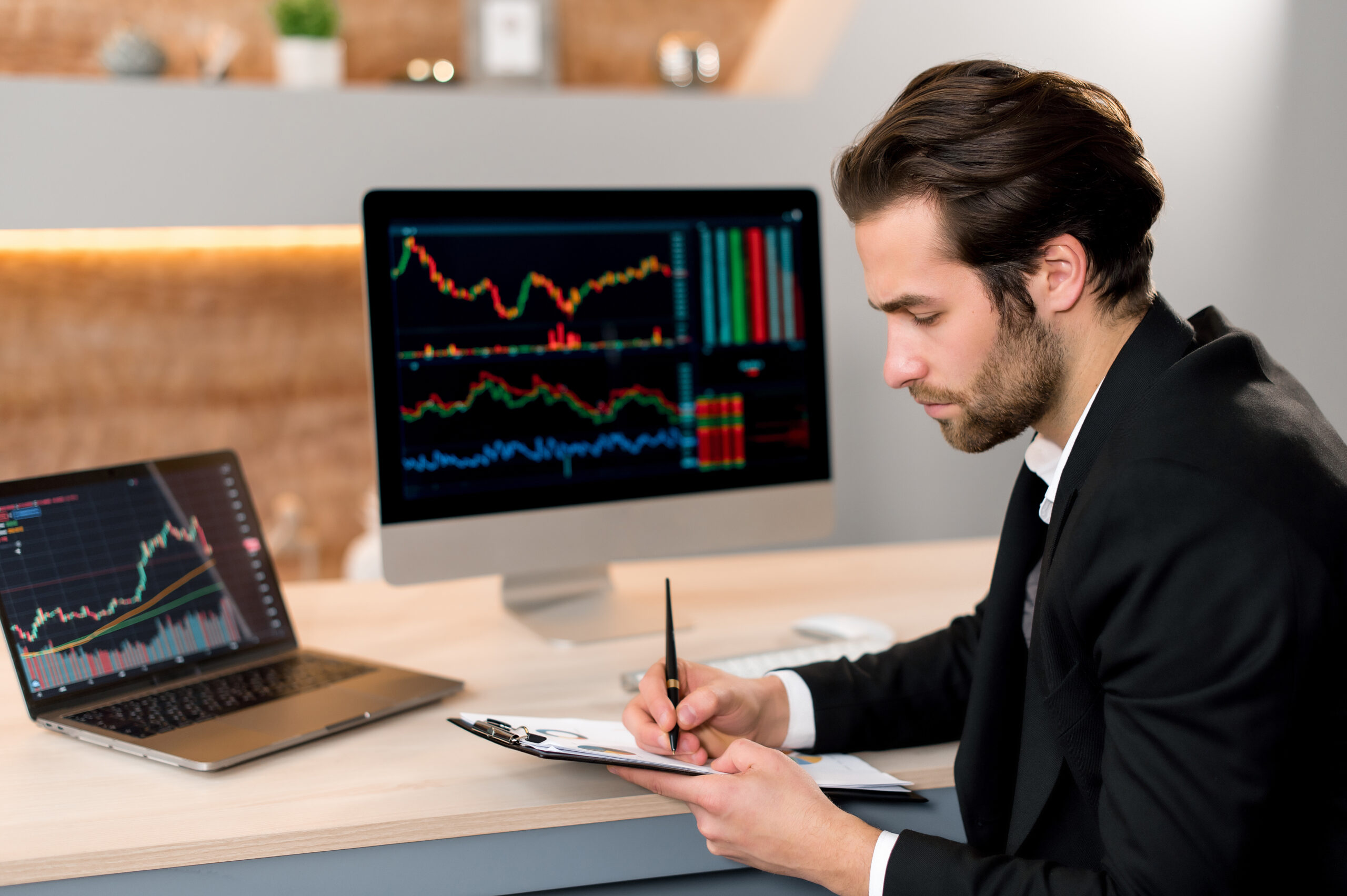 Stock market concept. Focused smart successful caucasian businessman, trader investor, broker, sits at a desk in a modern office, in formal suit, analyze trading charts, predicts profit