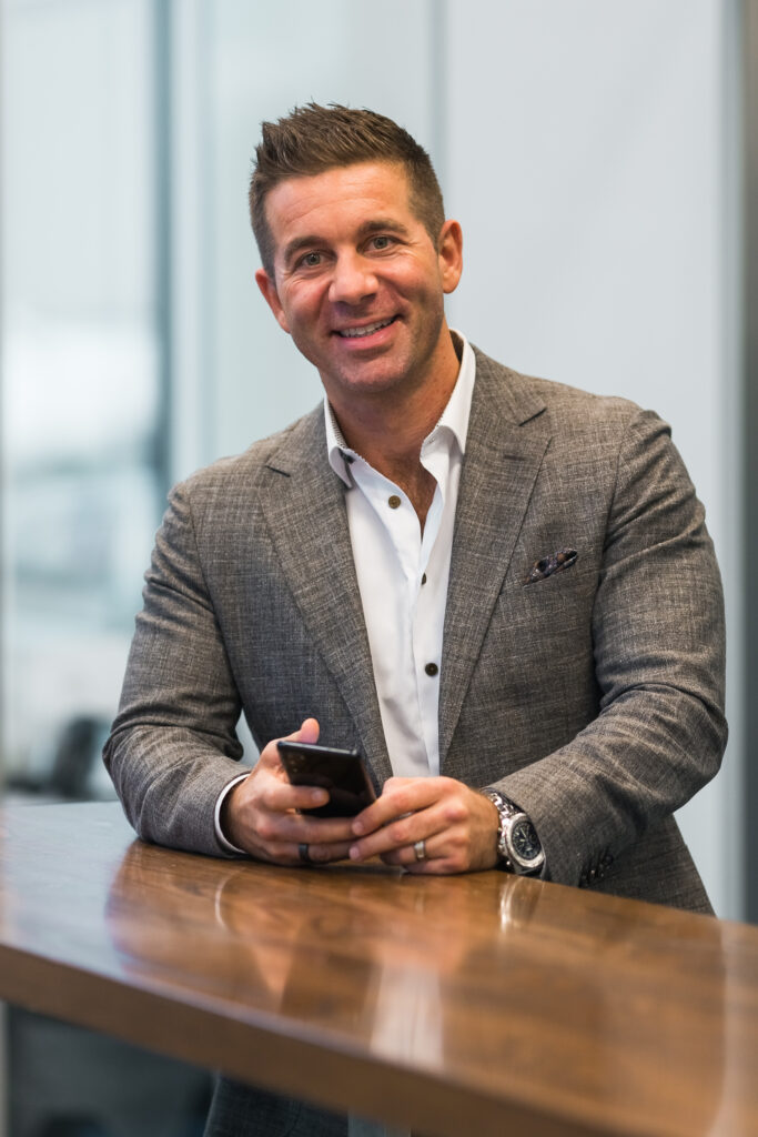 A man in a suit is smiling while holding a cell phone.