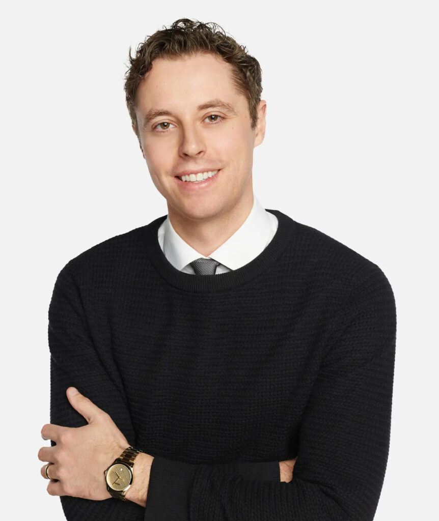 A smiling man in a black sweater and tie.
