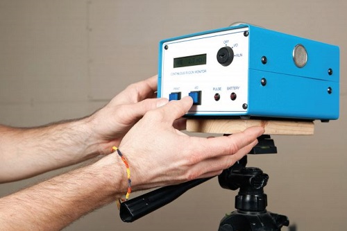 A person holding a blue electronic device on a tripod.