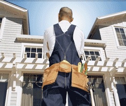 A man in overalls standing in front of a house.