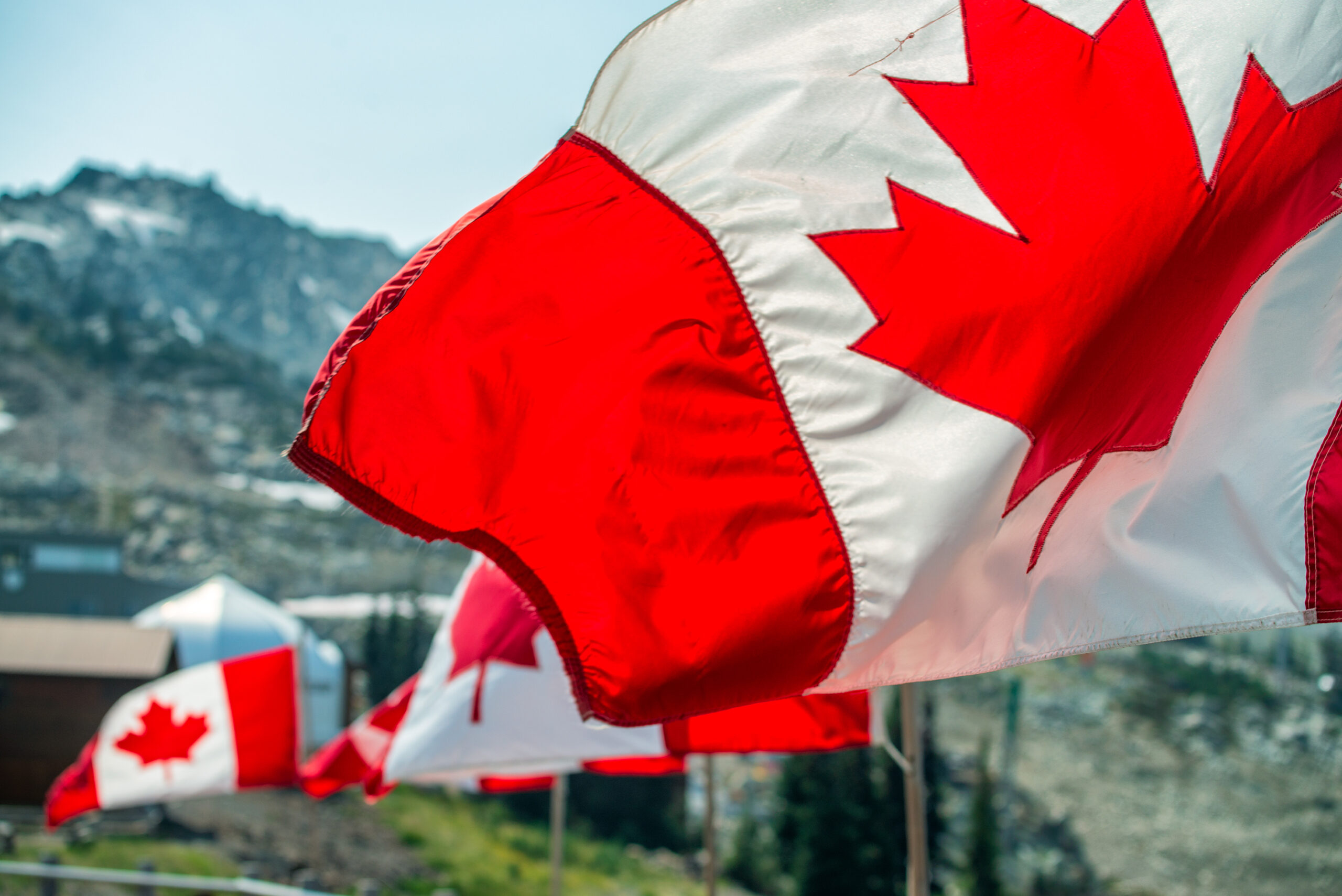 Canada,Flags,Waving,At,The,Wind,In,Mountain,Scenario.