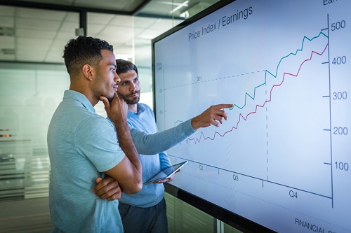 Two men pointing at a graph on a whiteboard.