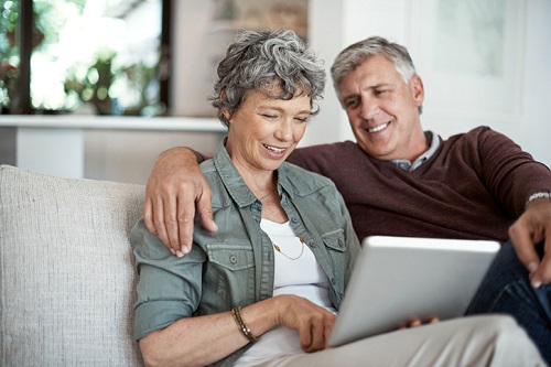 An older couple sitting on a couch looking at a tablet computer.
