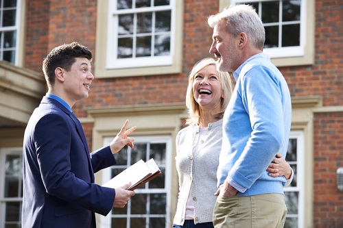 A realtor talking to a couple in front of a house.