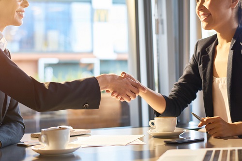 Two business women shaking hands at a table.