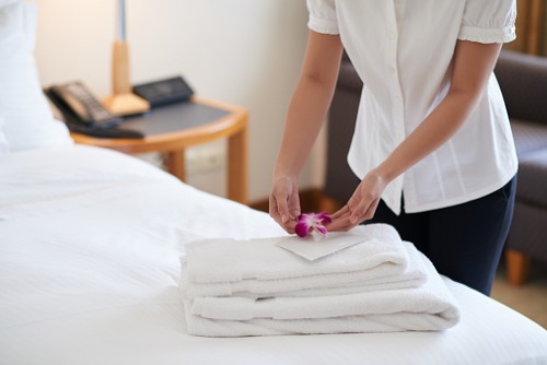 A woman is putting towels on a bed in a hotel room.