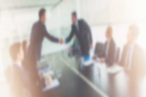 A blurry image of business people shaking hands at a conference table.