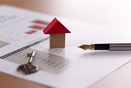 A house model on top of a piece of paper with a pen and key.