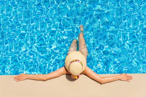 A woman in a hat is laying in a swimming pool.