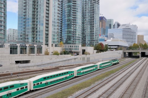 A green and white train passing through a city with tall buildings.