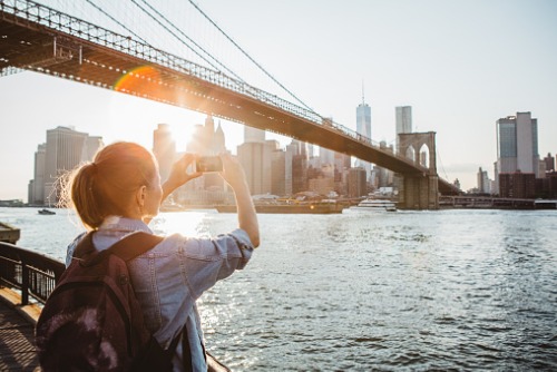 A woman taking a picture of the brooklyn bridge.