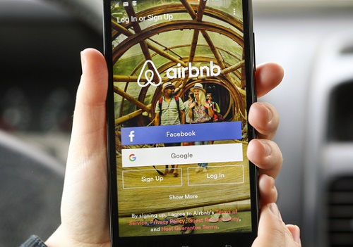 A person holding a cell phone with the airbnb app on it.