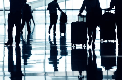 Silhouettes of people walking with luggage in an airport.