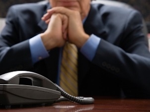 A man in a suit sits at a desk with a telephone.