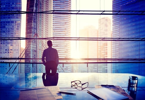 Silhouette of a businessman standing at a desk in front of a city skyline.